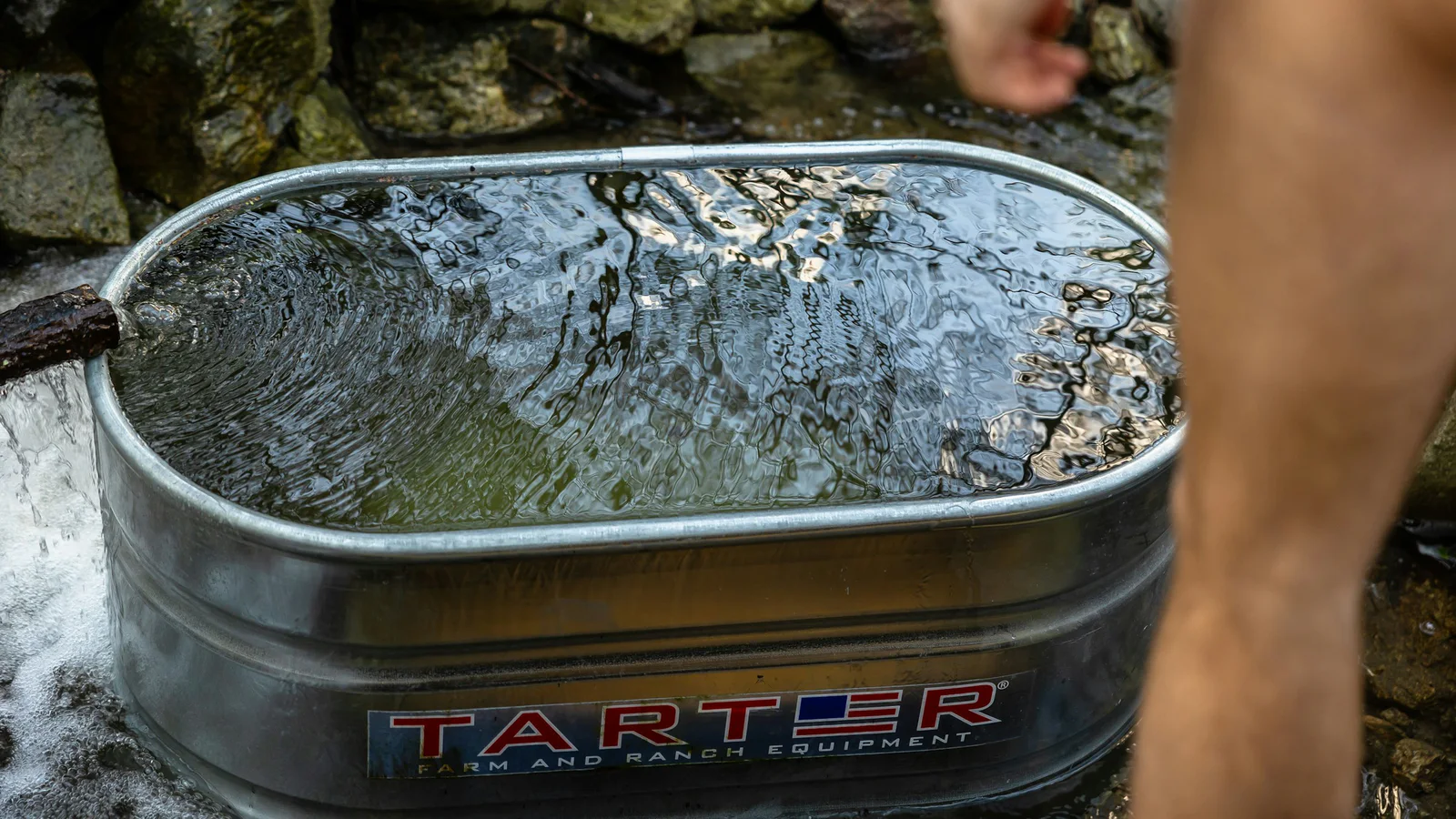 Outdoor metal tub filled with water beside a person preparing to enter