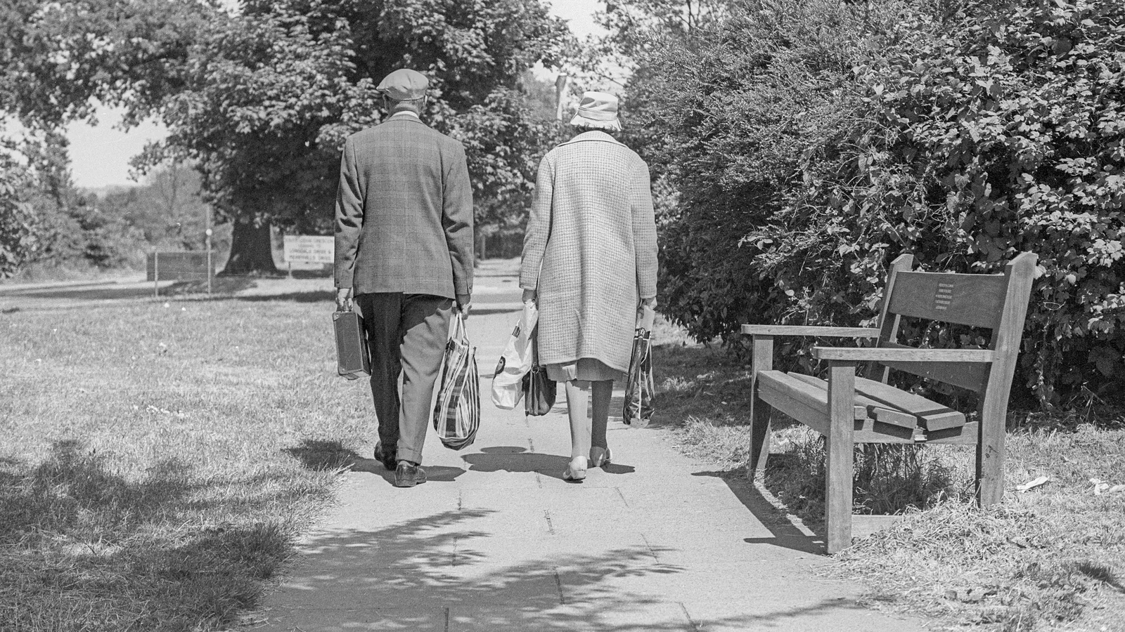 Black-and-white photograph of an elderly couple walking through a park